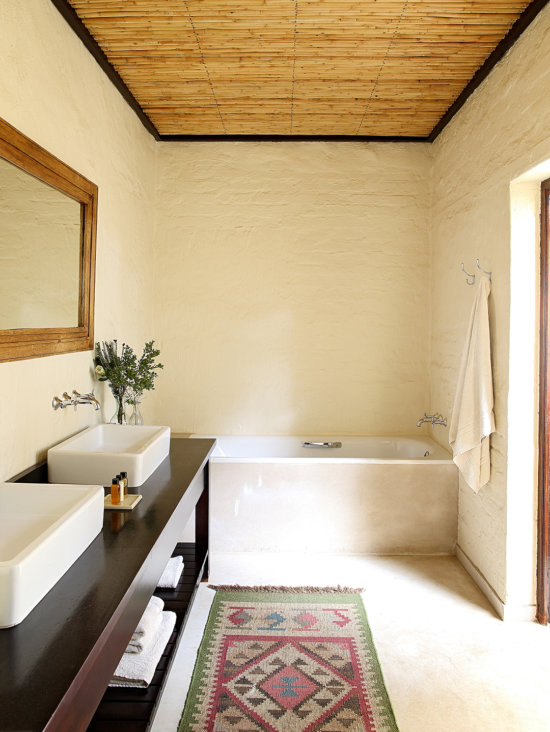 Elephant House bathroom with bath, double basins and floor rug.