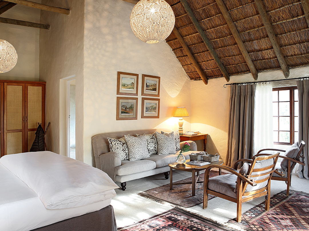 Sumptuous bedroom with king-size bed and sitting area under a thatched ceiling.