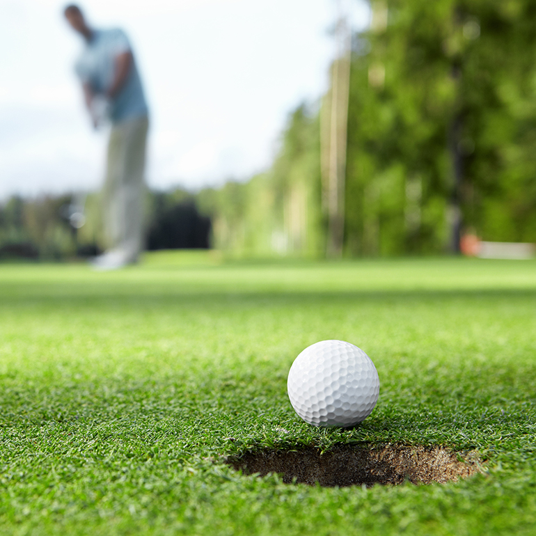 Golfer putting a golfball towards a hole on the green.