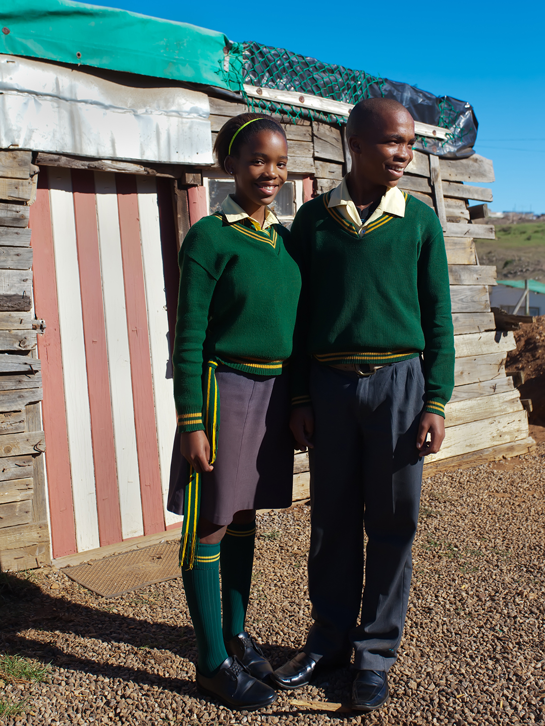 South African brother and sister proudly standing in their school uniforms in front of their home.
